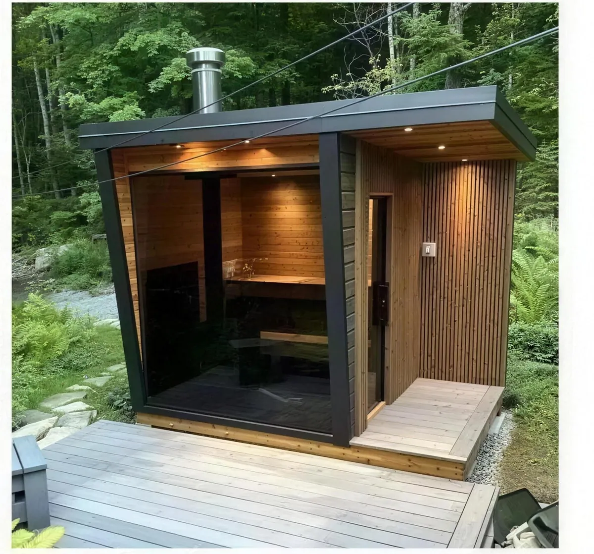 Kabin outdoor sauna kayu api dengan serombong dan fasad kayu gelap di laman berhutan